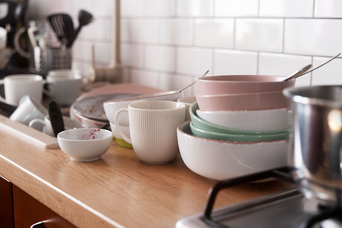 Dirty dishes piled up on a kitchen counter representing chores dumped on a lazy hubby by his wife on strike.