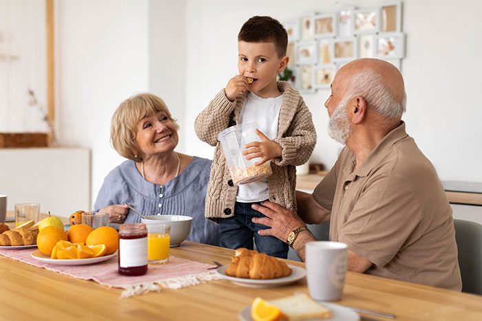 Grandparents and grandson enjoying breakfast together, highlighting lazy hubby inviting mom to help with chores.