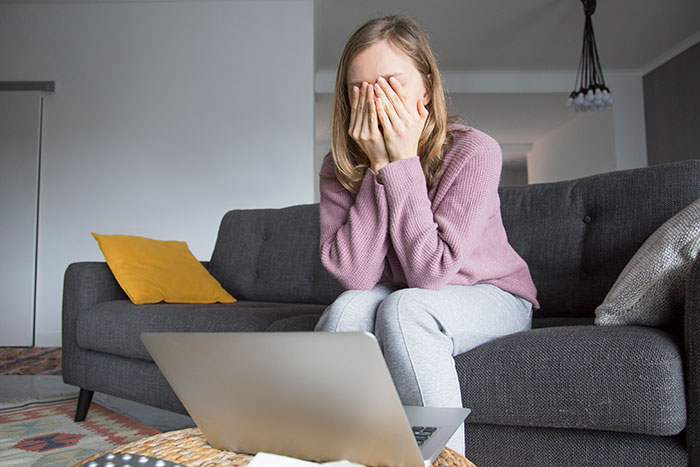 Woman sitting on a couch covering her face in distress, reflecting emotional struggle with postpartum boundaries.