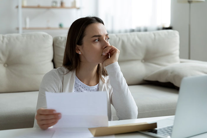 Woman sitting on couch, holding a letter and looking worried, reflecting on postpartum boundaries challenges.