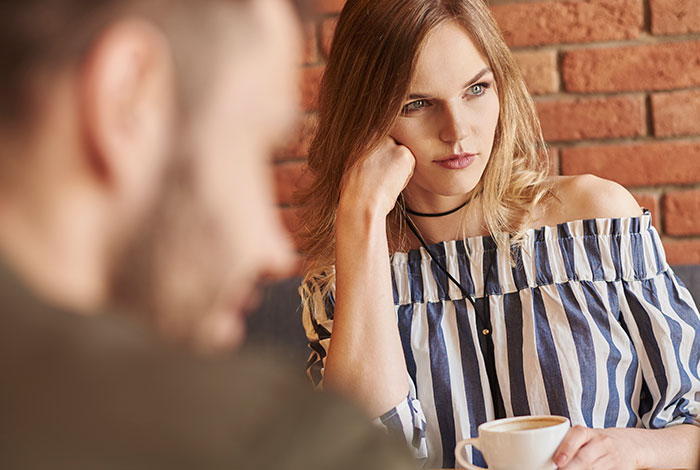 Woman looking suspiciously at a man across the table in a caf&eacute;, illustrating a MIL tries to catfish woman scenario.