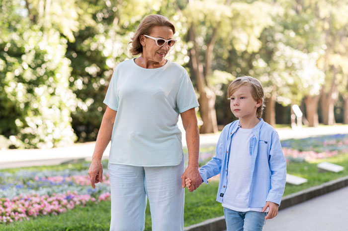 Older woman holding hands with young boy in park, representing granny pretending to be kid's guardian concept.