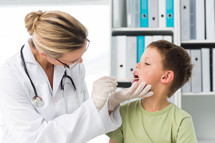 Doctor examining a young boy’s throat in a medical office, addressing throat pain and diagnostic concerns.