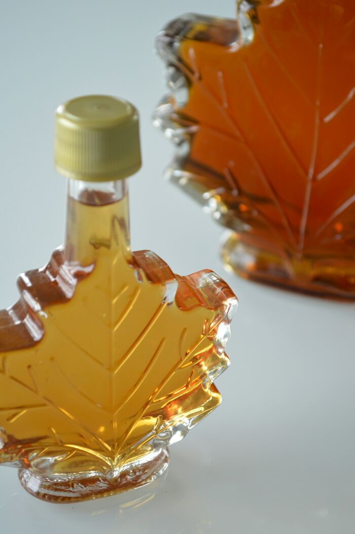 Two glass maple leaf-shaped bottles filled with amber liquid on a light surface, representing today I learned facts.