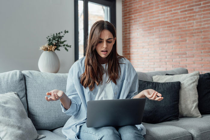 Woman sitting on couch looking confused while using a laptop, researching naming son Harry Potter ideas and options.