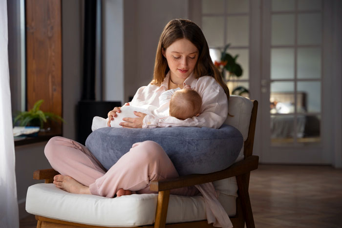 Mother sitting on chair with a nursing pillow, holding and feeding her baby son inspired by Harry Potter naming ideas