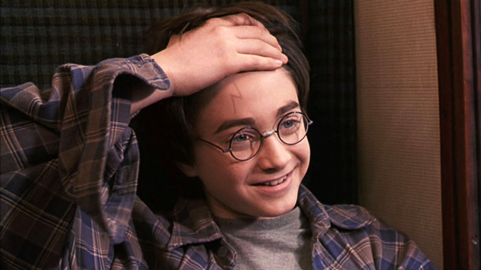 Young boy resembling Harry Potter smiling and touching forehead while sitting on a train, related to naming son Harry Potter.