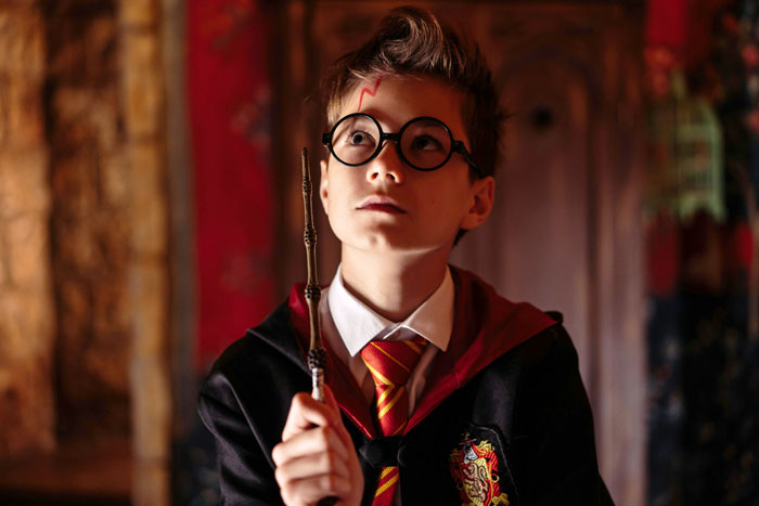 Young boy dressed as Harry Potter, holding a wand and wearing glasses with a lightning bolt scar on his forehead.