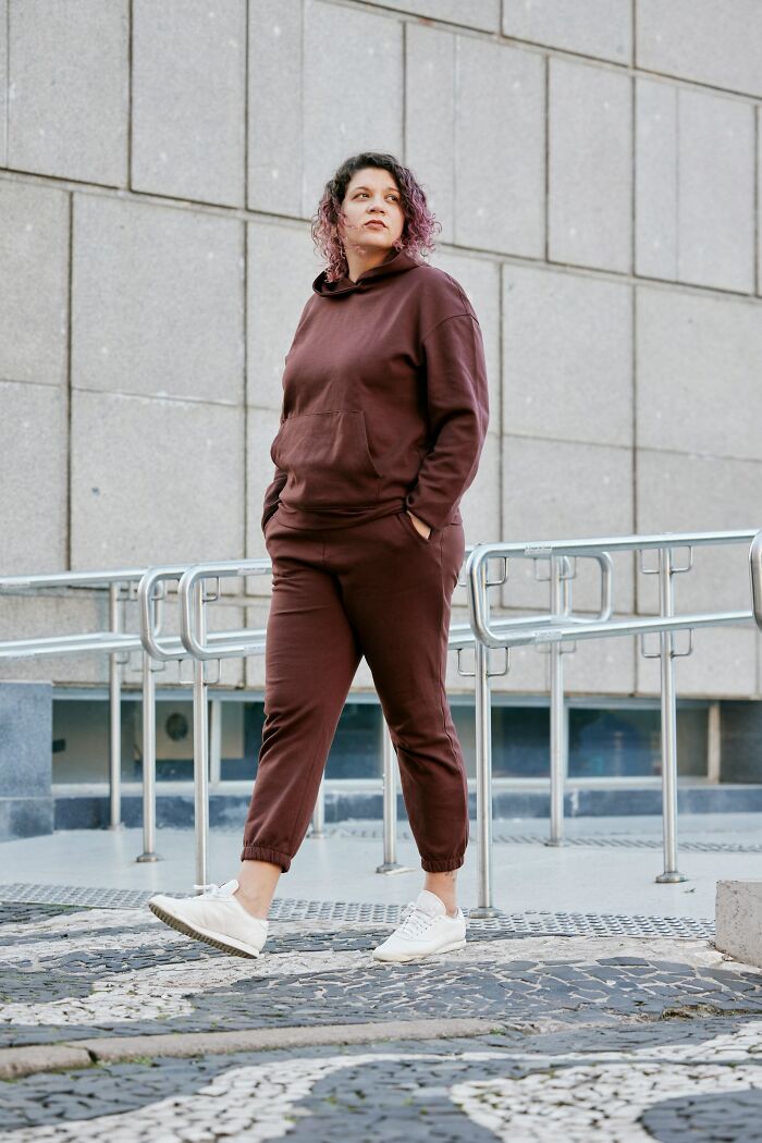Person wearing a brown tracksuit standing outdoors near a modern building, illustrating silent judgment of others behavior.