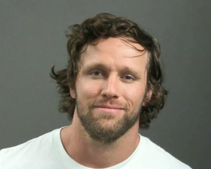 Russell Brand in a close-up portrait with a beard and curly hair, linked to disturbing charges and hot tub baptism news.