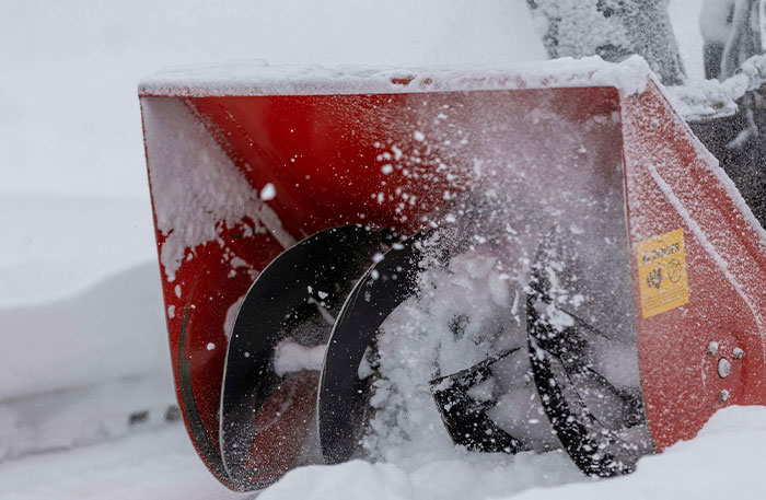 Close-up of a guy using a snowblower to clear snow, ensuring a neighbor&rsquo;s driveway is the only one snowed in.