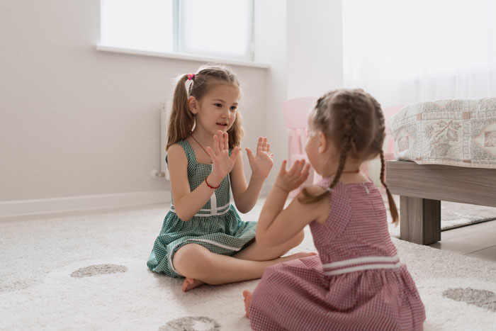 Two young girls playing hand clapping game indoors during a messy playdate in a bright, cozy room.