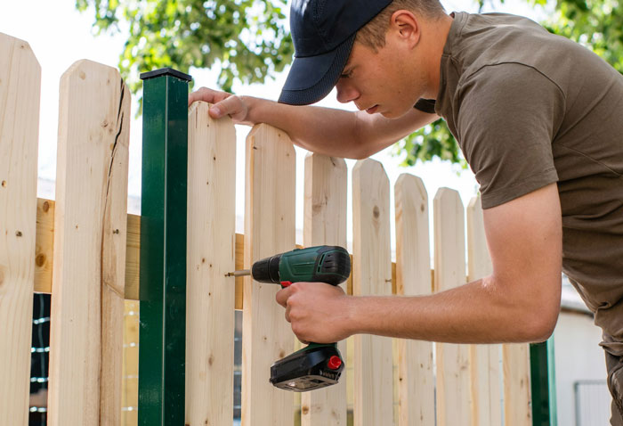 Man using cordless drill to build a wooden fence, representing neighbors dealing with living hedge property boundaries.