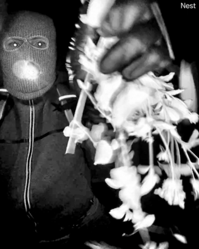 Person in a knitted mask holding a ransom note demanding bitcoin, captured in a dark, grainy surveillance image.