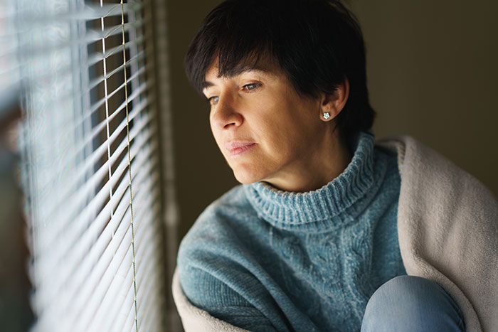 Woman in a blue sweater looking thoughtfully out a window, reflecting on refusing to lend her new snow blower.