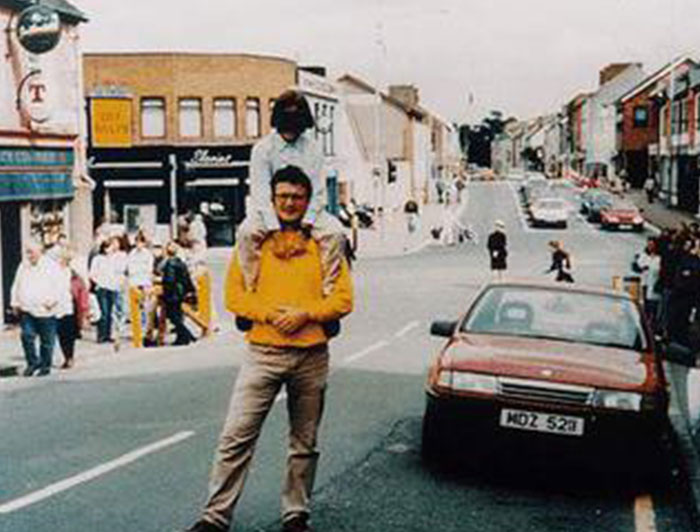 Man in yellow sweater carrying child on shoulders standing on busy street among powerful photos from around the world.