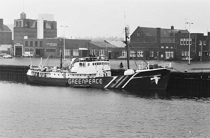 Black and white photo of Greenpeace ship docked at industrial port, a powerful photo from all over the world.