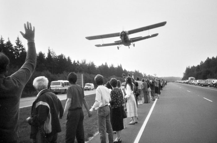 People standing along a road waving at a small airplane flying low, a powerful photo capturing a unique moment worldwide.