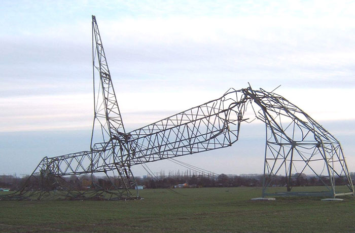 Collapsed electrical tower lying on a grassy field, showcasing a powerful photo of infrastructure damage from all over the world.