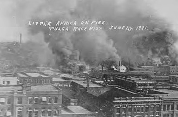 Black and white photo showing smoke rising over buildings during the Tulsa race riot, a powerful photo from history.