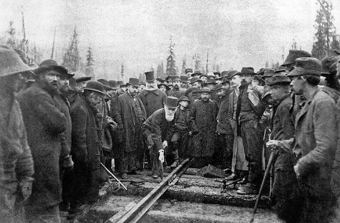 Historic black and white photo showing a large group of men gathered around a railway track during powerful moments worldwide.