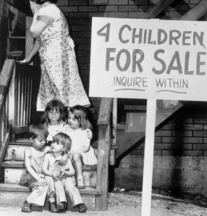 Black and white powerful photo showing four children sitting on steps next to a sign offering children for sale.