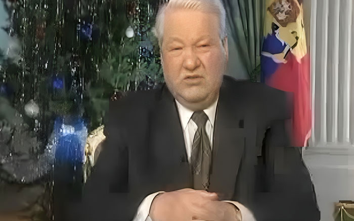 Man in a suit and tie sitting in an official room with a decorated Christmas tree and a flag behind him in a powerful photo setting.