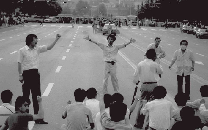 Group of people protesting on a wide street, raising fists and blocking cars in a powerful photo from all over the world.