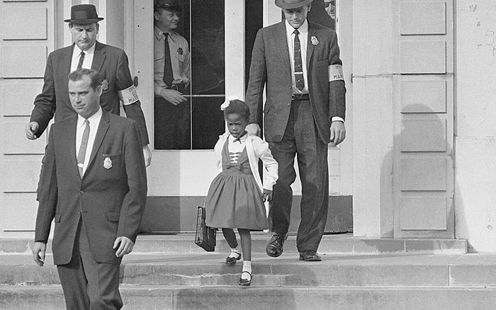 Historic powerful photo showing a young African American girl escorted by men in suits outside a government building.