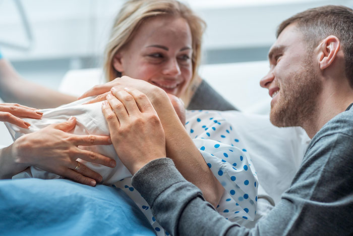 Pareja sonriente sosteniendo a un bebé recién nacido en un hospital, reflejando momentos de drama instantáneo y tensión.
