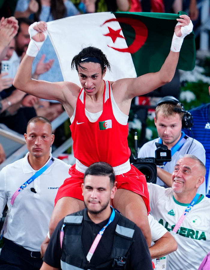 Imane Khelif celebrating victory while holding Algerian flag, highlighting controversy over Y chromosome gene admission.