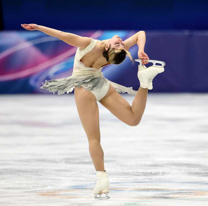 US figure skater performing a spiral move on ice during a competition with a colorful background and white costume.