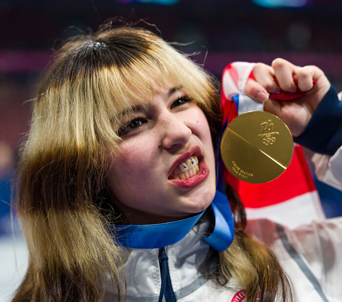 US figure skater holding broken gold medal with a grimace during celebration at a sporting event.