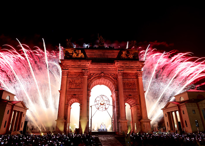 Fireworks light up the night sky above a grand arch during the Olympic Village event capturing the heated athlete atmosphere.