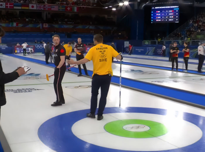 Olympics curling match in progress with players discussing strategy on ice during a major event after Canada cheating accusations.