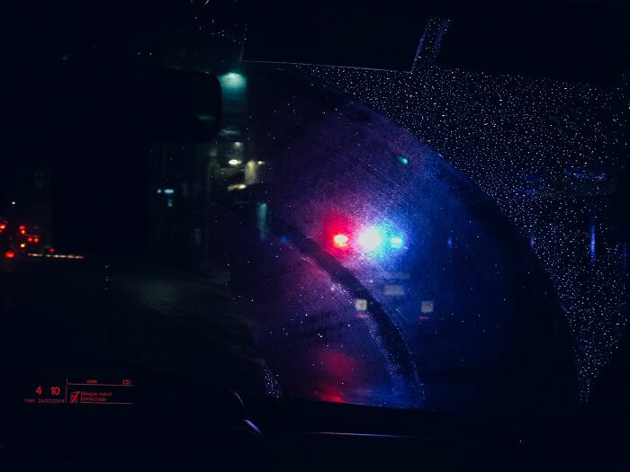 Police lights flashing outside a rainy car window at night, evoking wild dating experiences that made people question reality.