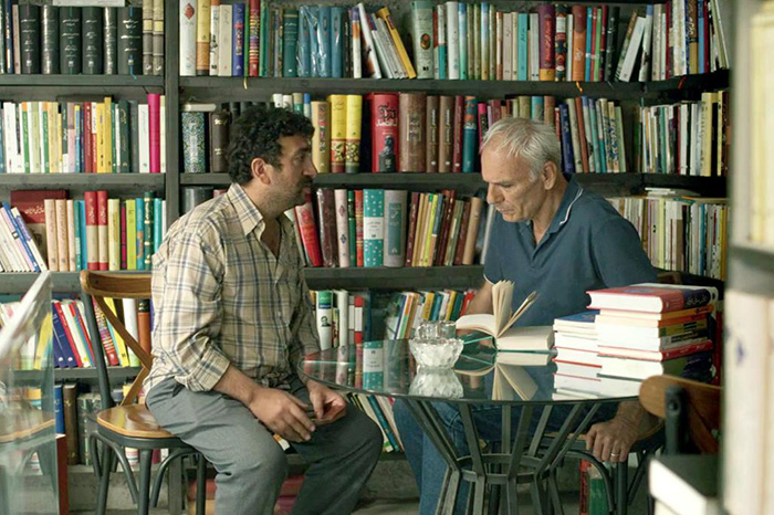 Two men discussing while sitting at a glass table in a bookstore, related to Oscar nominated movies 2026.