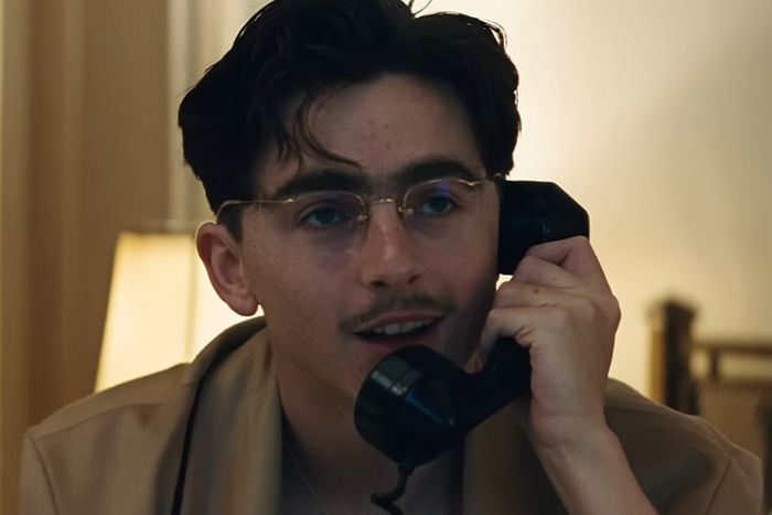 Young man with glasses talking on a black vintage phone in a dimly lit room from Oscar nominated movies 2026.