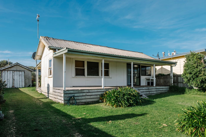 Small inherited house with front porch and green lawn, symbolizing a man wanting half of girlfriend’s property deed.