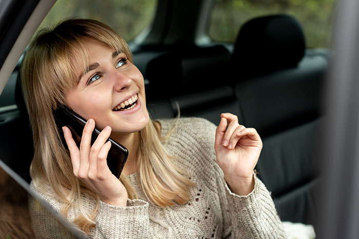 Young woman smiling and talking on phone in car while partner looks annoyed, trying to mute music nearby
