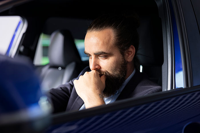 Man sitting in a car looking annoyed while partner faceplate mutes music with a frustrated expression.