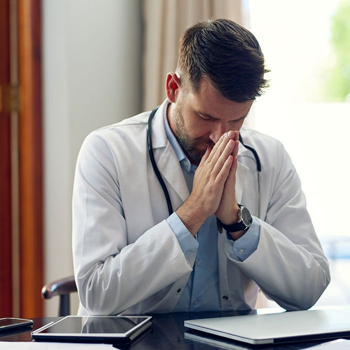 Doctor with a stethoscope looking stressed at his desk, highlighting challenges patients create for doctors and nurses.