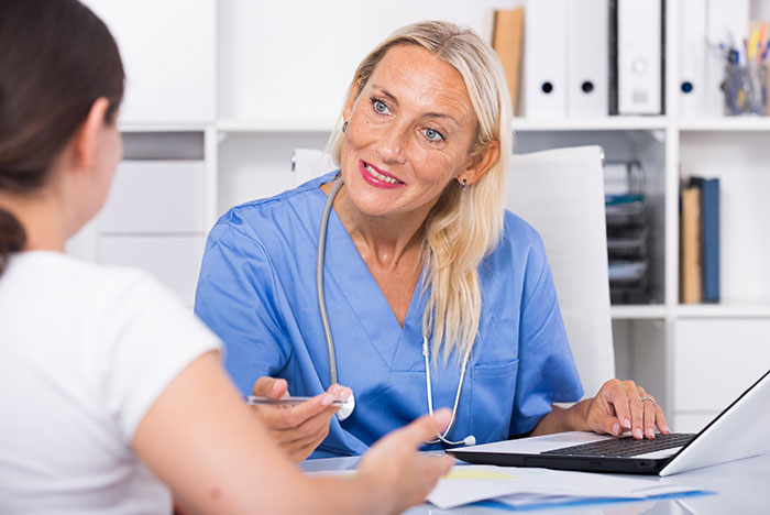 Female nurse in blue scrubs talking to a patient, illustrating common patient behaviors that affect doctors and nurses.