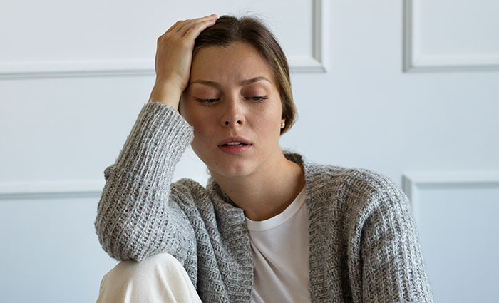 Woman in gray sweater sitting indoors looking stressed, illustrating common things patients do that affect doctors and nurses.