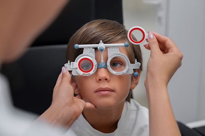 Child at an eye exam with a doctor adjusting the trial frame, illustrating patient actions affecting doctors and nurses.