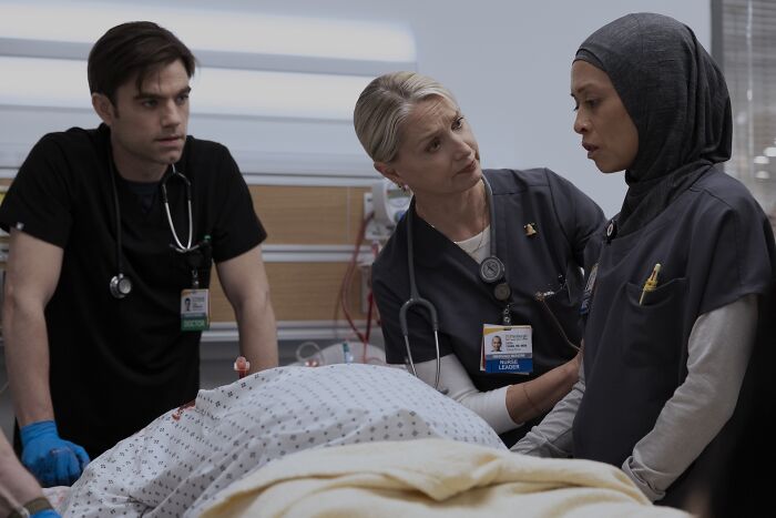 Three medical professionals in scrubs and stethoscopes attend to a patient in a hospital room scene from The Pitt Season 2. Three medical professionals in scrubs and stethoscopes attend to a patient in a hospital room scene from The Pitt Season 2.