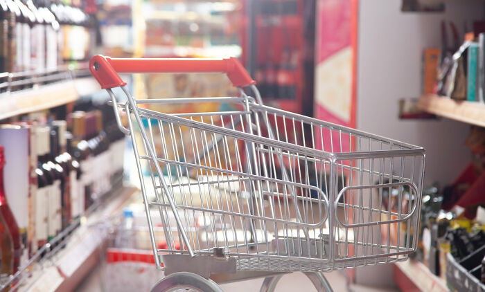 Empty shopping cart in a grocery aisle, illustrating surprisingly petty things people secretly judge others for.