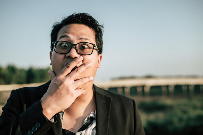 Man with glasses covering mouth in outdoor setting, reflecting on surprisingly petty things people secretly judge others for