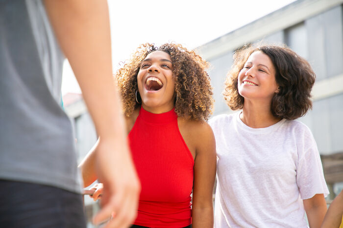 Two women laughing and chatting outdoors, showcasing expressions related to surprisingly petty things people secretly judge.
