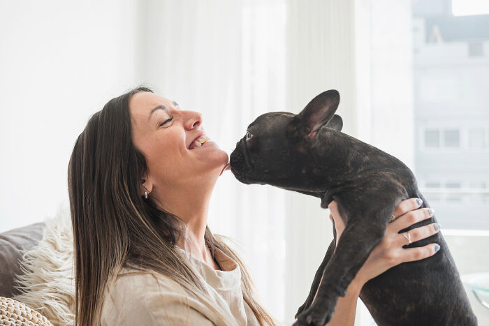 Woman smiling as she holds a French bulldog close, showing surprisingly petty things people secretly judge others for.